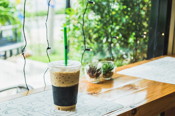 Iced coffee in a plastic cup on a wooden table at the cafe. Cold espresso in the coffee shop with copy space. Beverage glass frozen in the restaurant. Food sales busy interior decoration vintage.