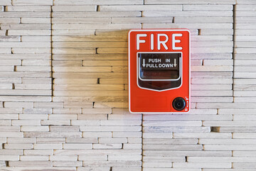 Fire alarm press button on white concrete brick wall background in the hotel corridor with copy space. Emergency concept