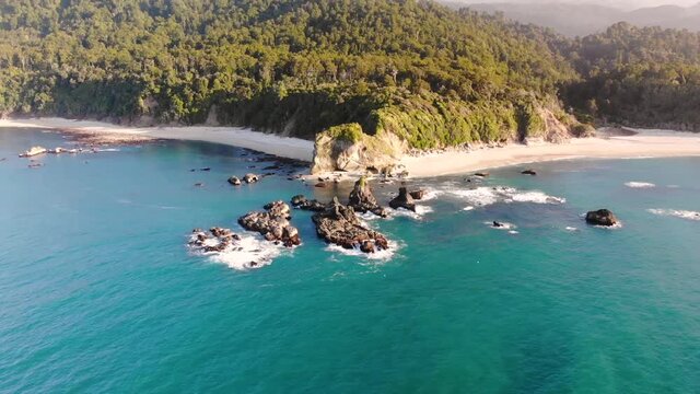Afternoon Sunlight Over The Beautiful Pristine Water Of The Monro Beach In South Island, New Zealand With Lush Tropical Paradise In The Background - aerial drone