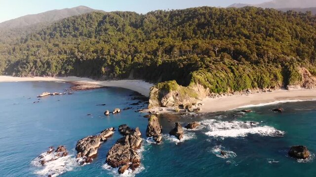 Drone Flying Over The Rocks Surrounded By Turquoise Blue Sea Near The Shore In Monro Beach, New Zealand - aerial