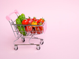 Pink shopping cart full of vegetables on pink background