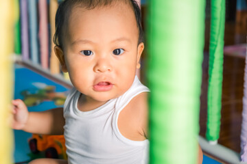 Cute little asian baby boy relaxing and looking up camera in the crib at home. Nursery for young children. Breastfeeding or early childhood development concept