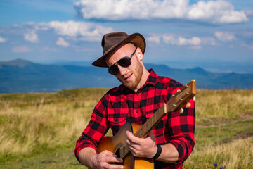 Naklejka na ściany i meble Camping holiday. Young Man Traveler with guitar relaxing outdoor with mountains on Summer vacations. Lifestyle hiking concept.