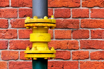 Yellow gutter downpipe and red brick wall as urban background.