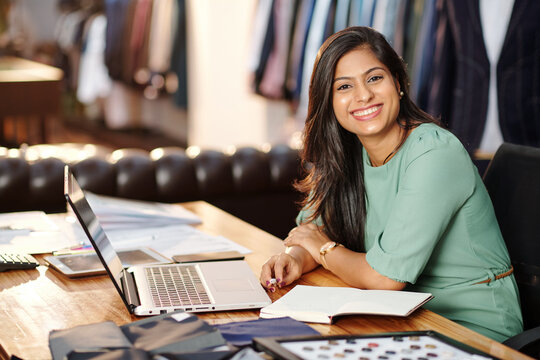 Portrait of happy young Indian atelier owner working on laptop
