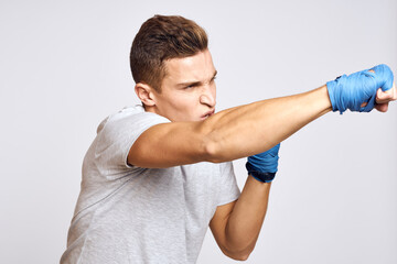 sporty male boxer in blue gloves practicing punches on a light background cropped view