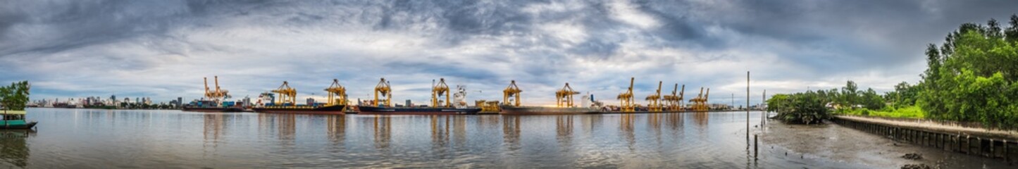 Fototapeta premium Panorama photo of harbor with anchored ship. Container cargo freight ship with working crane bridge at shipyard in for logistic transportation import and export at Asia haven port background, Thailand