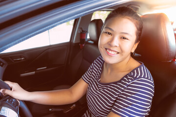 Happy businesswoman while driving the car and smiling on her morning commute to work. Asian young woman on her luxury automobile on the road trip.