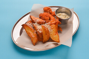 Chicken nuggets with baked potatoes, cheese on top and sauce. Served on a metal tray over pastel blue background.