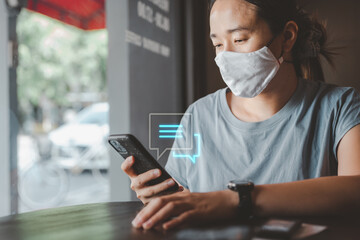 smart asian female new lifestyle Wear a face mask and use a smartphone typing, chatting conversation in chat box icons pop up. Social media marketing concept. during the Coronavirus COVID-19 pandemic.