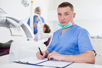 Concentrated male stomatologist recording diagnosis of patient at modern dental clinic