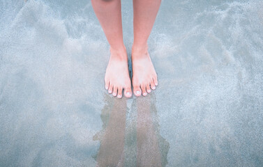 Above view the feet of woman standing alone on the beach with the waves of the sea. Footprints on...