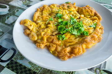 Above view of omelet with coriander in white ceramic plate on the table at the restaurant. Omelette with onion it's egg fry popular traditional Thai Asian style food. Top view, Top-down