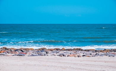Beautiful wave with blue sky over the horizon hitting rock coast background. Tropical colorful sand from the landscape sea. The holiday summer the beach vacation concept.