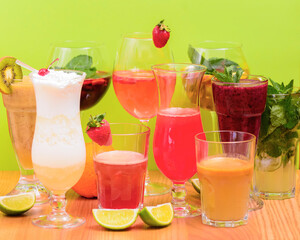 Summer drinks with fruit juice and ice. Refreshing summer beverages in different glasses over green background.