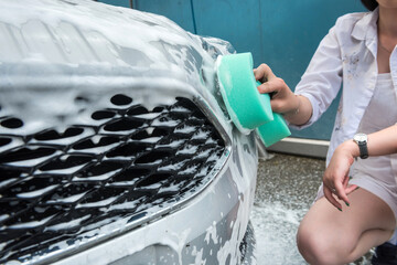 hand hold  sponge with white foam over the car for washing