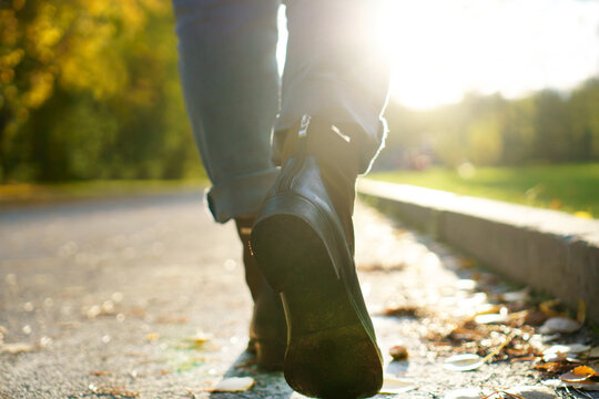 The girl walks along the road in the autumn city park. Autumn women's shoes on the legs of a girl. The girl is wearing blue jeans.