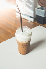 Iced coffee in a plastic cup on a wooden table at the cafe. Cold espresso in the coffee shop with copy space. Beverage glass frozen in the restaurant. Food sales busy interior decoration vintage.