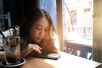 Asian young brunette woman sitting in modern cafe interior near huge window 