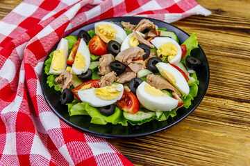 Tasty tuna salad with lettuce, black olives, eggs and fresh vegetables on wooden table