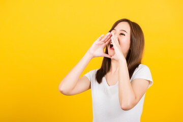 Asian happy portrait beautiful cute young woman teen standing big shout out with hands next mouth giving excited positive looking to side isolated, studio shot on yellow background with copy space