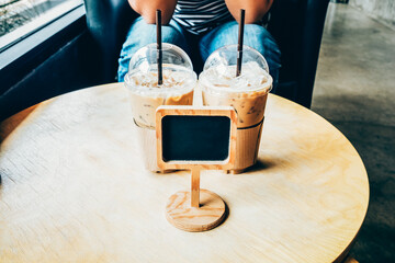Iced coffee in a plastic cup on a wooden table at the cafe. Cold espresso in the coffee shop. Beverage glass frozen in the restaurant. Food sales busy interior decoration vintage.