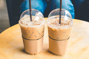 Iced coffee in a plastic cup on a wooden table at the cafe. Cold espresso in the coffee shop. Beverage glass frozen in the restaurant. Food sales busy interior decoration vintage.