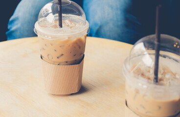 Iced coffee in a plastic cup on a wooden table at the cafe. Cold espresso in the coffee shop with copy space. Beverage glass frozen in the restaurant. Food sales busy interior decoration vintage.
