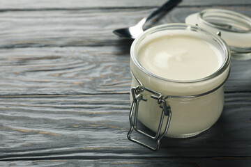 Glass jar of sour cream yogurt and spoon on gray wooden background