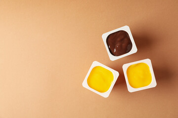 Plastics cups of yogurt on brown background, top view