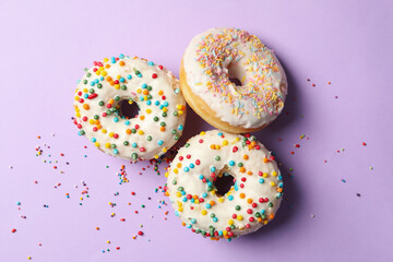 Three tasty donuts on violet background, top view