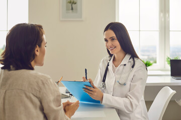 Fototapeta premium Young smiling female doctor discusses the diagnosis with a patient in a medical office.