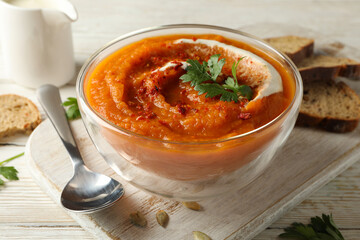 Composition with bowl of pumpkin soup on white wooden background, close up