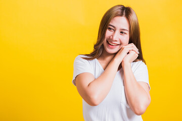 Fototapeta na wymiar Portrait Asian Thai beautiful happy young woman smiling, screaming excited keeps two hands together near the face and looking to side, studio shot isolated on yellow background, with copy space