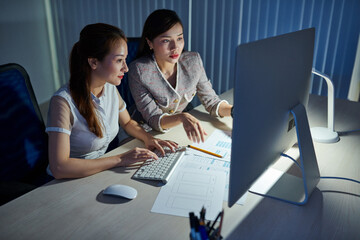 Young Vietnamese UI designer and project manager working in office late at night trying to finish project within deadline