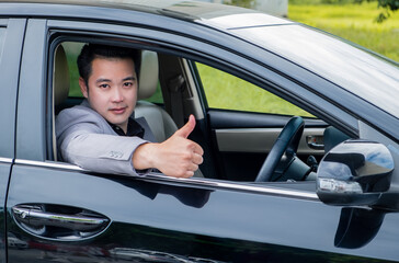 Fototapeta na wymiar Happy businessman while driving car and smiling on his morning commute to work. Handsome Asian young man his thumbs up on luxury automobile in the road trip.