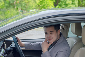 Happy businessman while driving the car and smiling on his morning commute to work. Executive handsome Asian young man on his luxury automobile on the road trip.