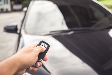 Businessman opens his luxurious car door with a modern remote control key. The young man is locking the automobile with the security system. Keyless in male hand.