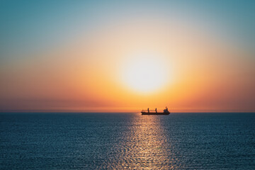 Rising sun over blue sea and silhouette of a transport ship
