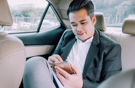 Happy businessman using smartphone calling while driving the car on his morning commute to work. Handsome Asian young man touching mobile phone communication on his luxury automobile on the road trip.