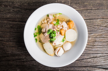 Noodles of Thai style clear soup in traditional ceramic bowl on old wooden table. Top view from above