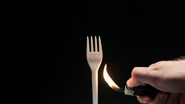 Hot flame gas lighter burns white disposable plastic fork. Say no to plastic concept.