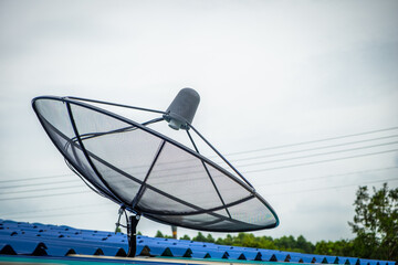 Satellite TV antenna on blue sky background with copy space. Cable dish above the roof of the house. Communication technology in the digital world concept.