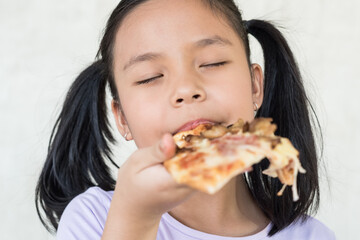 Mmm, so delicious! dark haired little asia girl eats slice of Italian pizza, keeps eyes closed from pleasure, enjoys nice taste, has good appetite, dressed in casual purple shirt, eating concept.