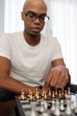 Smart young Black man playing chess at home and making first movement