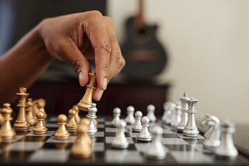 Close-up image of Black man moving golden queen chess piece