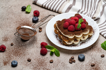 portion of Classic tiramisu dessert with raspberries on grey concrete background