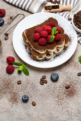 portion of Classic tiramisu dessert with raspberries on grey concrete background