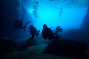 Fototapeta na wymiar Scuba divers black silhouettes in a blue cave making bubbles