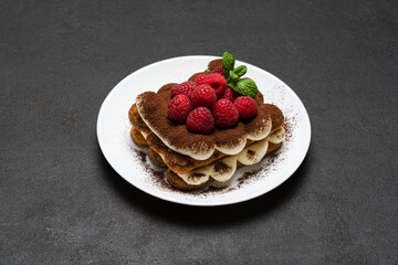 portion of Classic tiramisu dessert with raspberries on dark concrete background